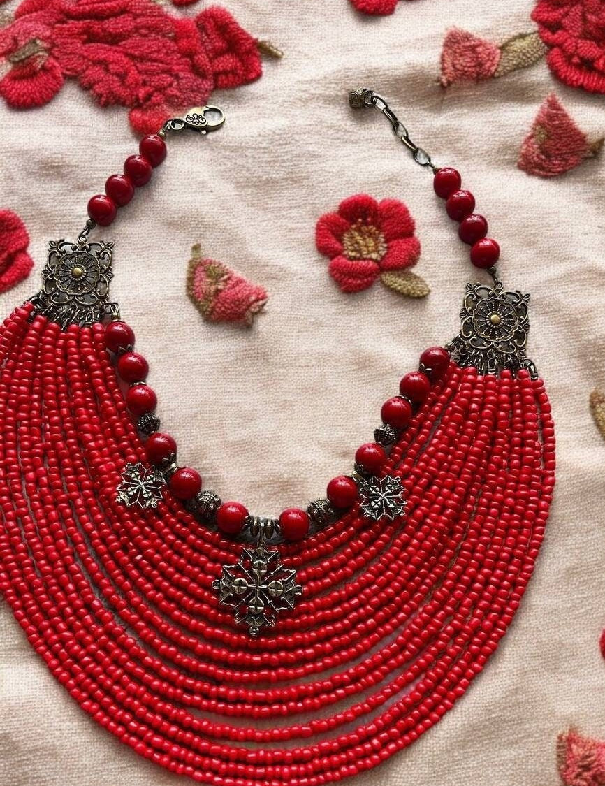 Ukrainian red bead necklace with crosses, crafted with glass and acrylic beads, bronze fittings, and brass charms on fabric background.
