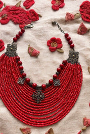 Ukrainian red bead necklace with crosses, crafted with glass and acrylic beads, bronze fittings, and brass charms on fabric background.