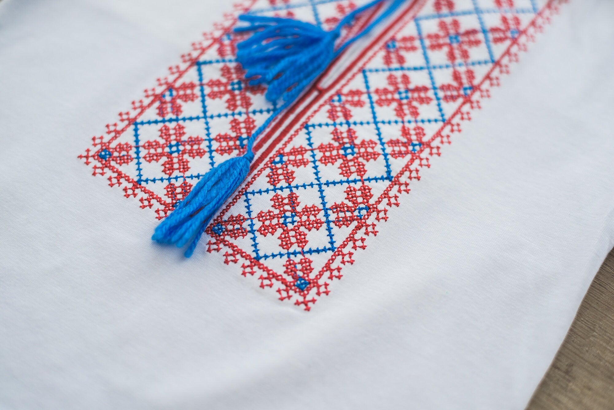 Close-up of Ukrainian vyshyvanka embroidery, featuring red and blue traditional patterns on a white fabric with tassels.