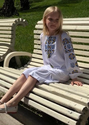 Girls' Ukrainian Vyshyvanka dress with Trident embroidery, traditional boho style, sitting on a park bench.