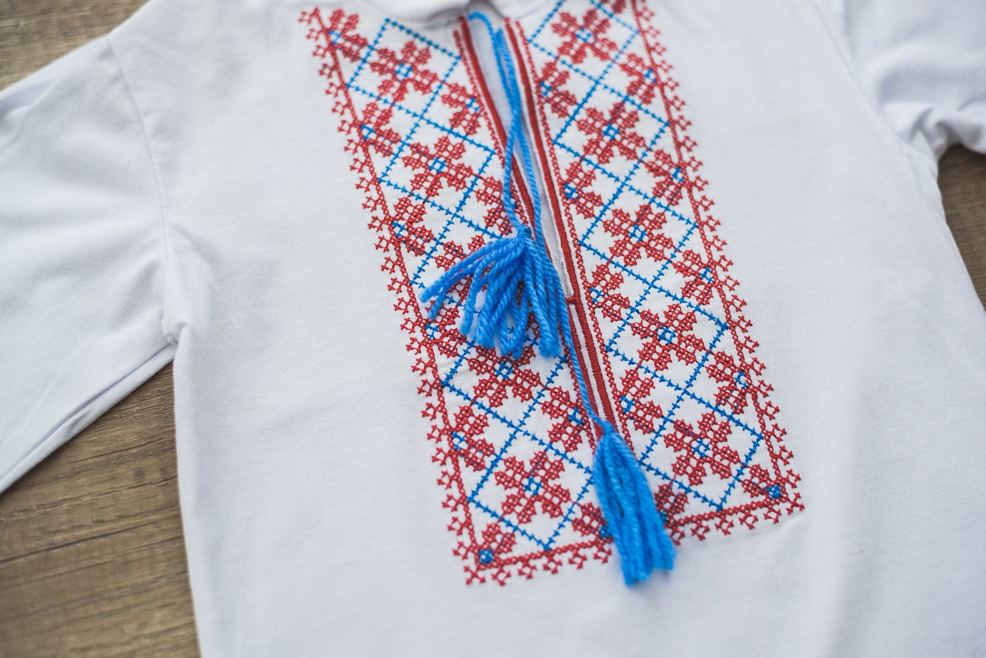 Traditional Ukrainian vyshyvanka for boys with red and blue embroidery on white fabric, ideal for cultural events and holidays.