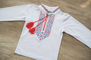 Boys Ukrainian vyshyvanka embroidered shirt with red and blue designs, suitable for babies and toddlers, on a wooden background.