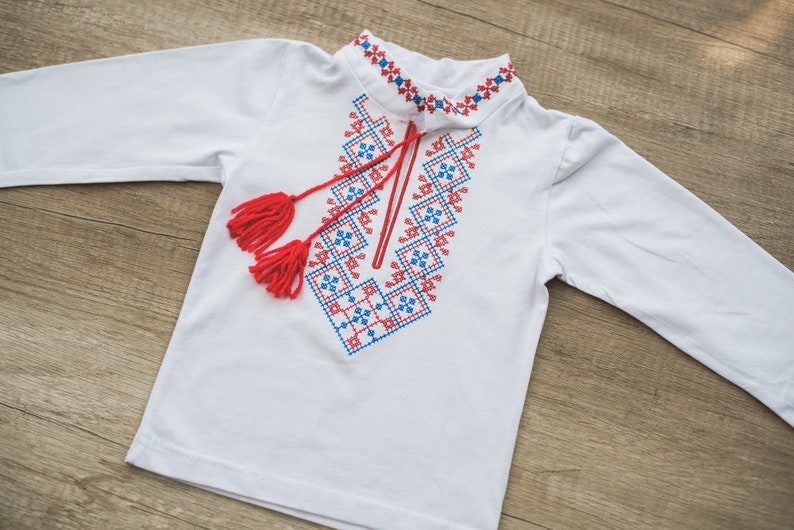Boys Ukrainian vyshyvanka embroidered shirt with red and blue designs, suitable for babies and toddlers, on a wooden background.