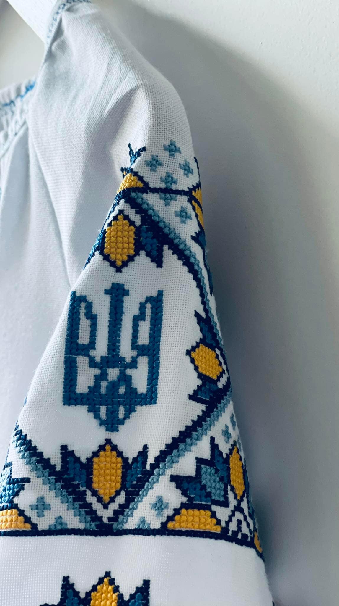 Embroidered sleeve detail of Ukrainian Vyshyvanka dress with Tryzub symbol in blue and yellow cross-stitch pattern.
