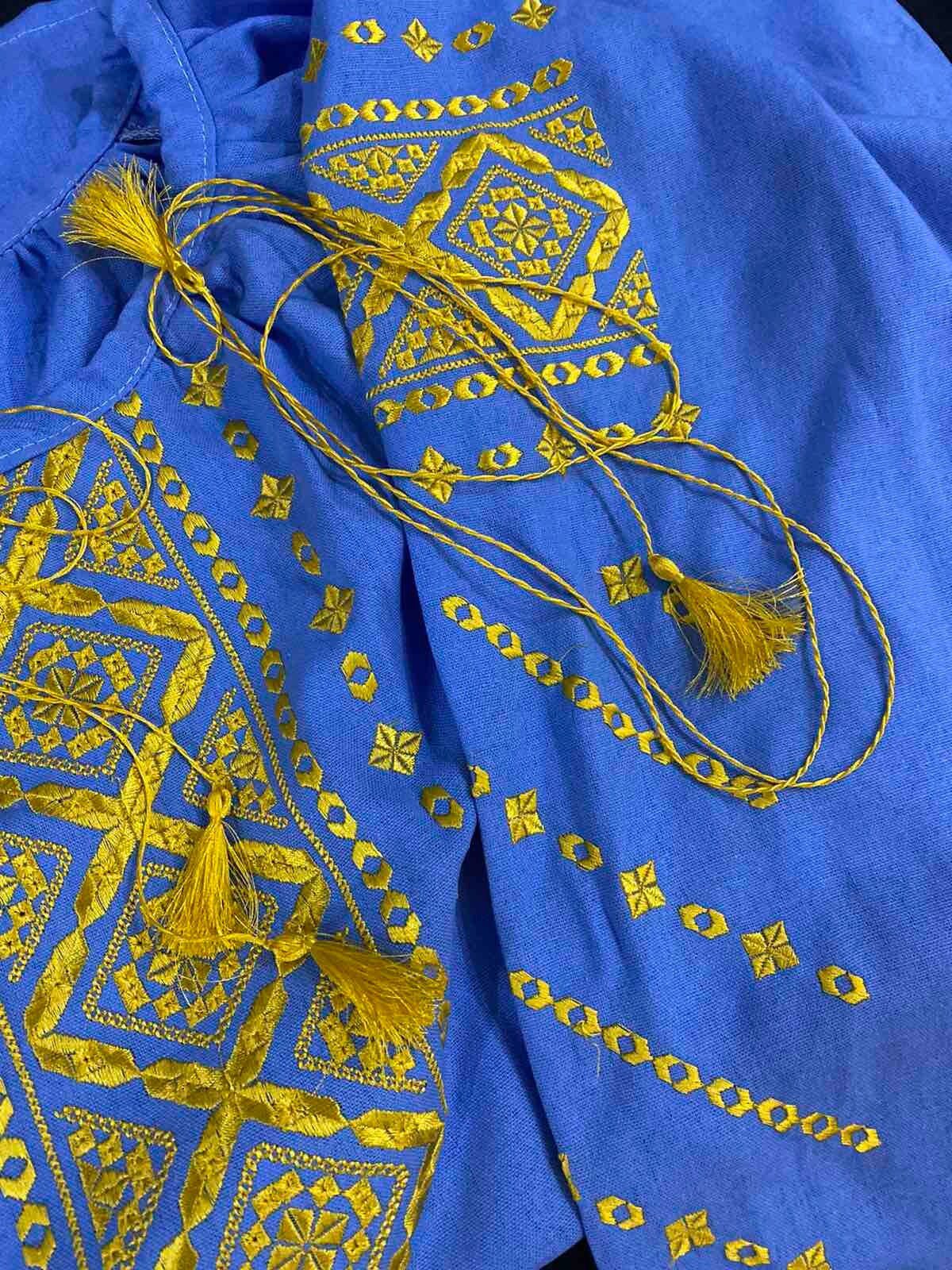 Vibrant blue and gold embroidered blouse, boho Ukrainian vyshyvanka style with tassels, showcasing intricate folk art patterns.