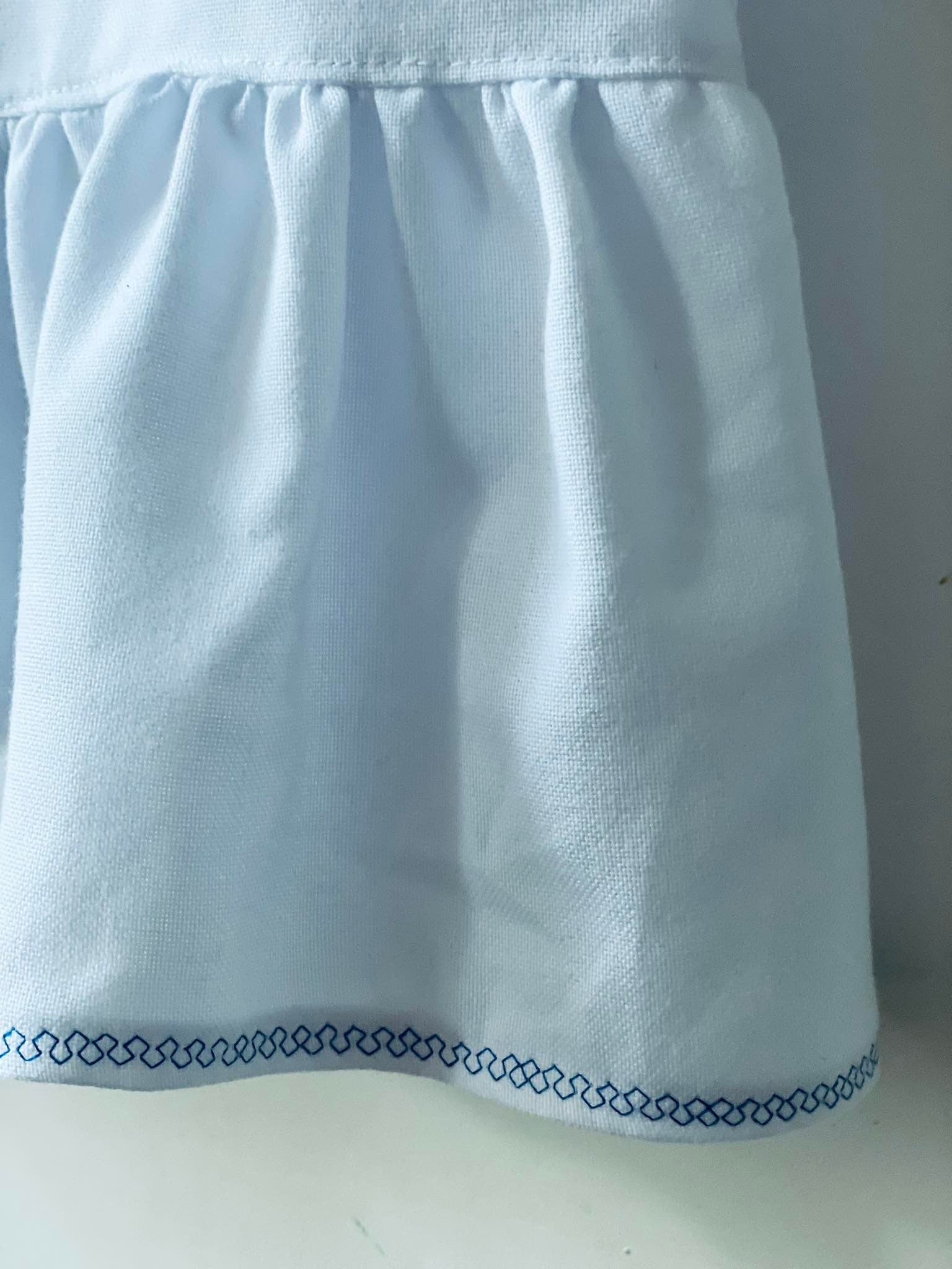 Close-up of the embroidered hem on a Ukrainian Vyshyvanka dress for girls, featuring delicate blue stitching on soft white cotton fabric.