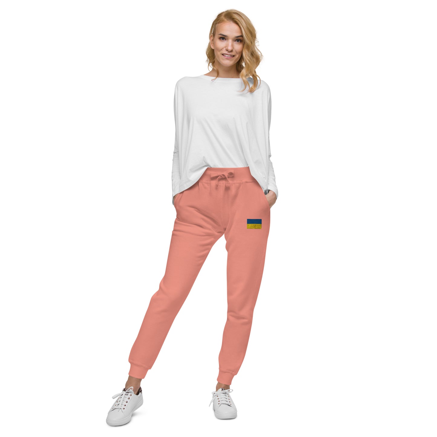 Woman wearing Ukrainian Flag fleece sweatpants in coral, paired with a white top and sneakers, showcasing casual style and comfort.