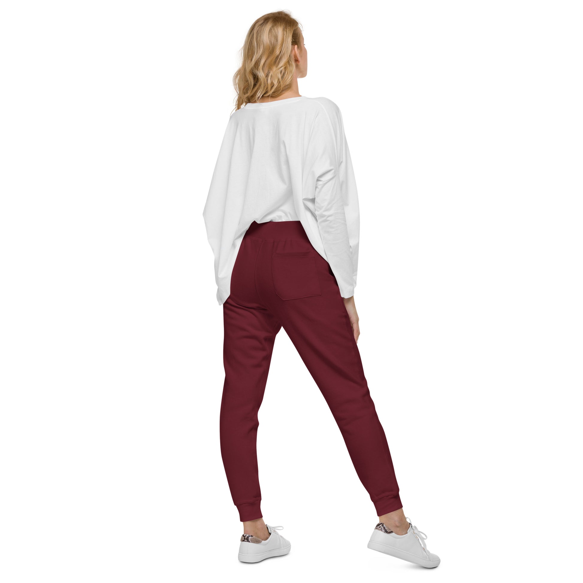 Woman wearing maroon sweatpants and white top, standing with back view, showcasing stylish casual outfit with sneakers.