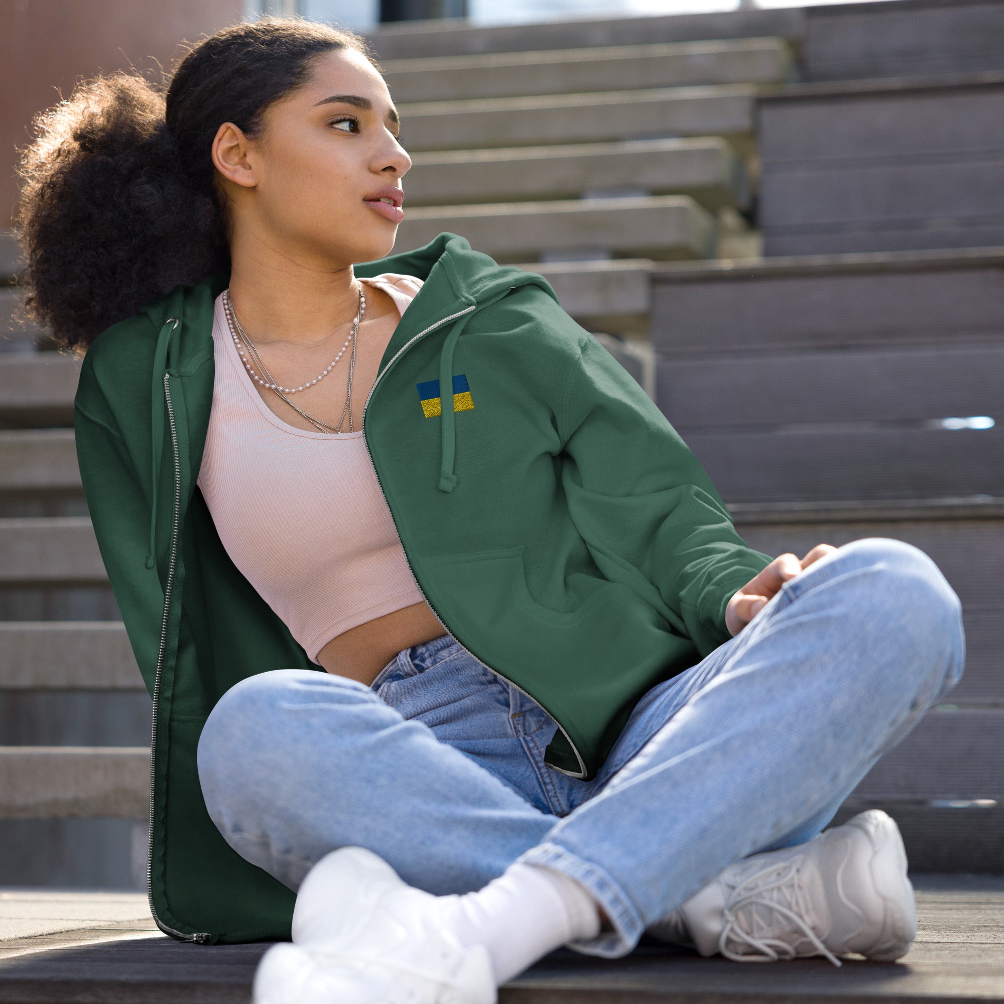 Woman wearing Ukrainian Flag fleece zip-up hoodie sitting on steps, showcasing cozy and stylish design for versatile layering.