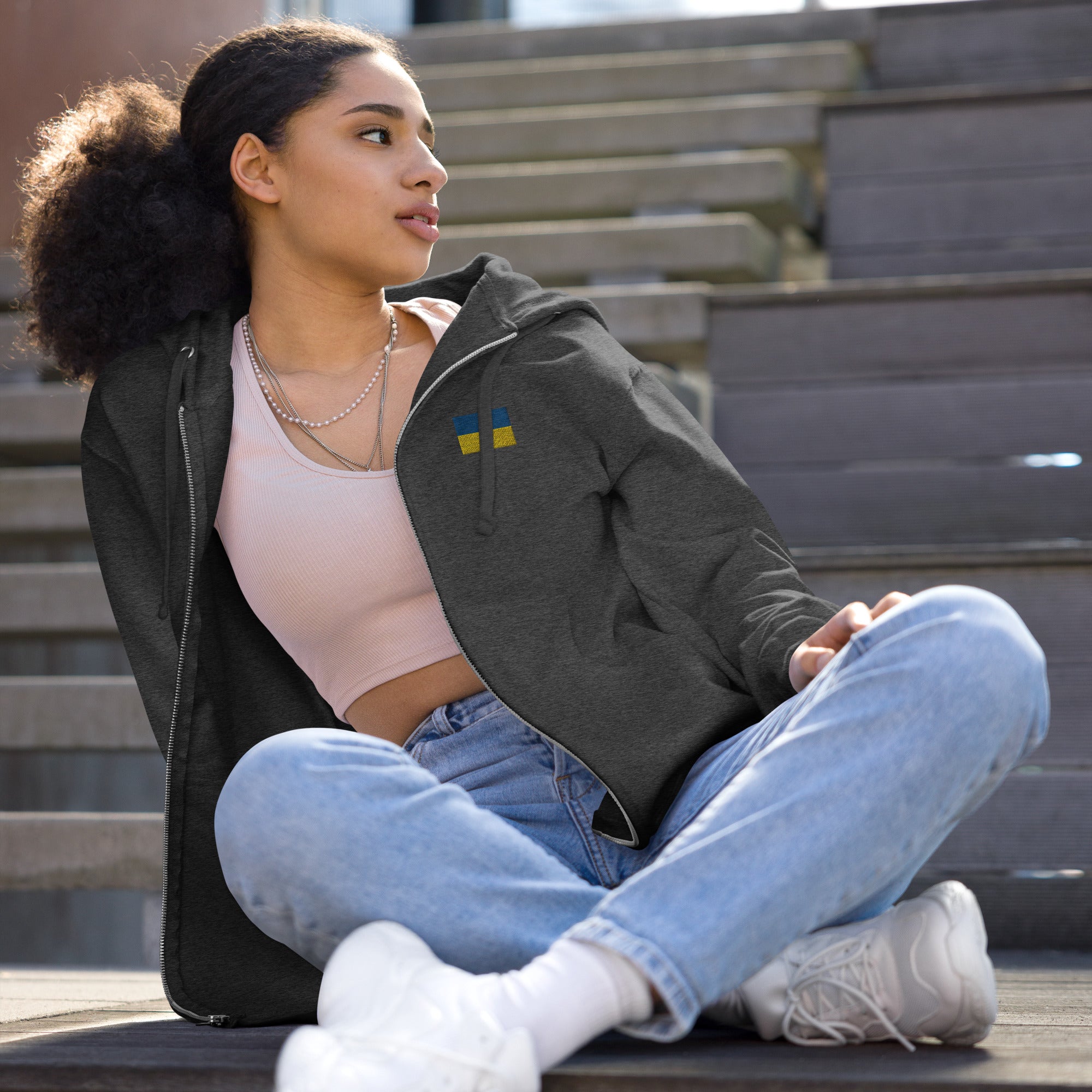 Woman wearing Ukrainian Flag fleece zip-up hoodie from Ukrainian Vibe Trizub Collection, sitting on stairs, casual outfit.