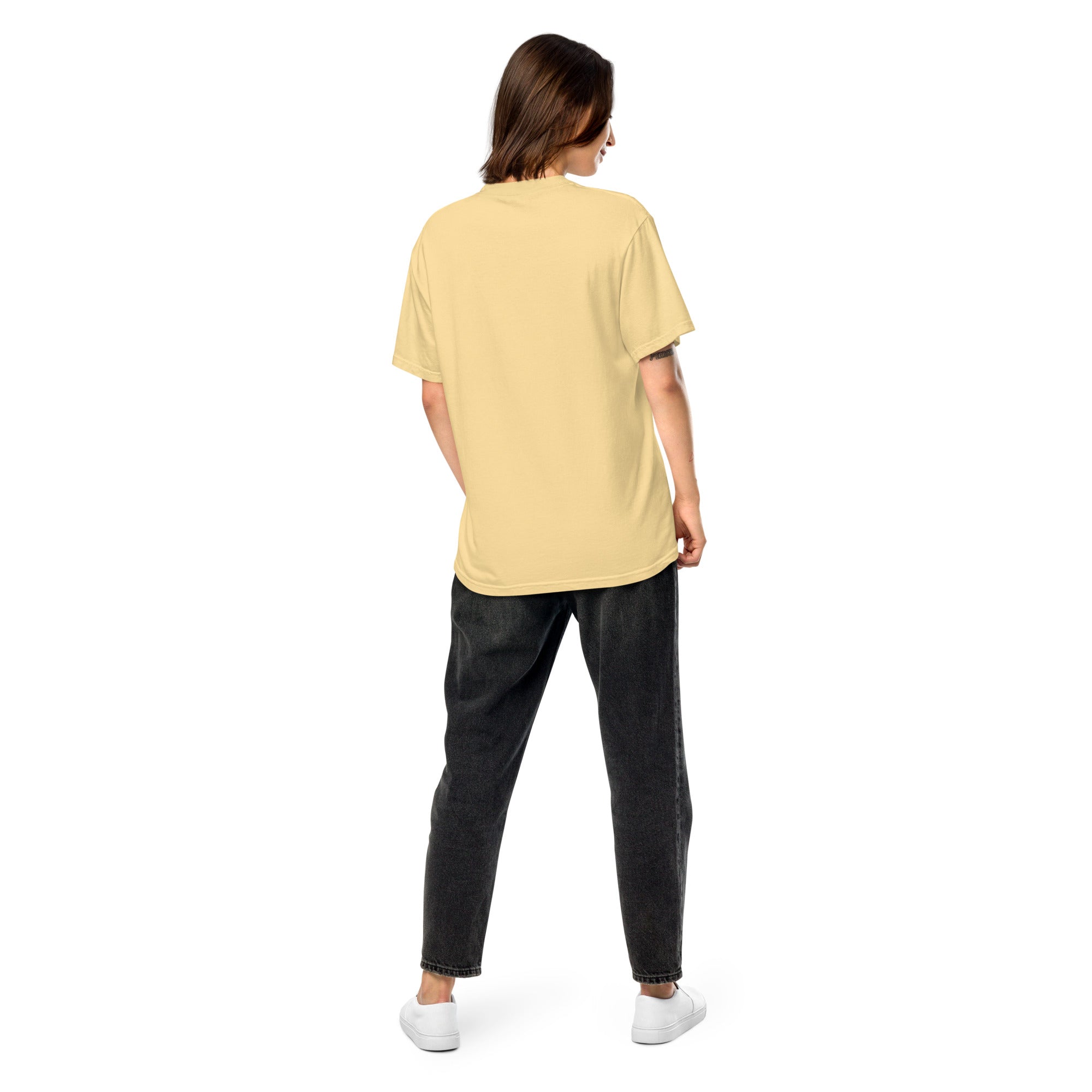 Back view of woman wearing Ukrainian Vibe Trizub Collection garment-dyed heavyweight t-shirt in soft beige, paired with black jeans and white sneakers.
