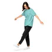 Woman in Ukrainian Vibe Trizub Collection garment-dyed teal t-shirt, black jeans, and white sneakers showcasing relaxed fit and style.