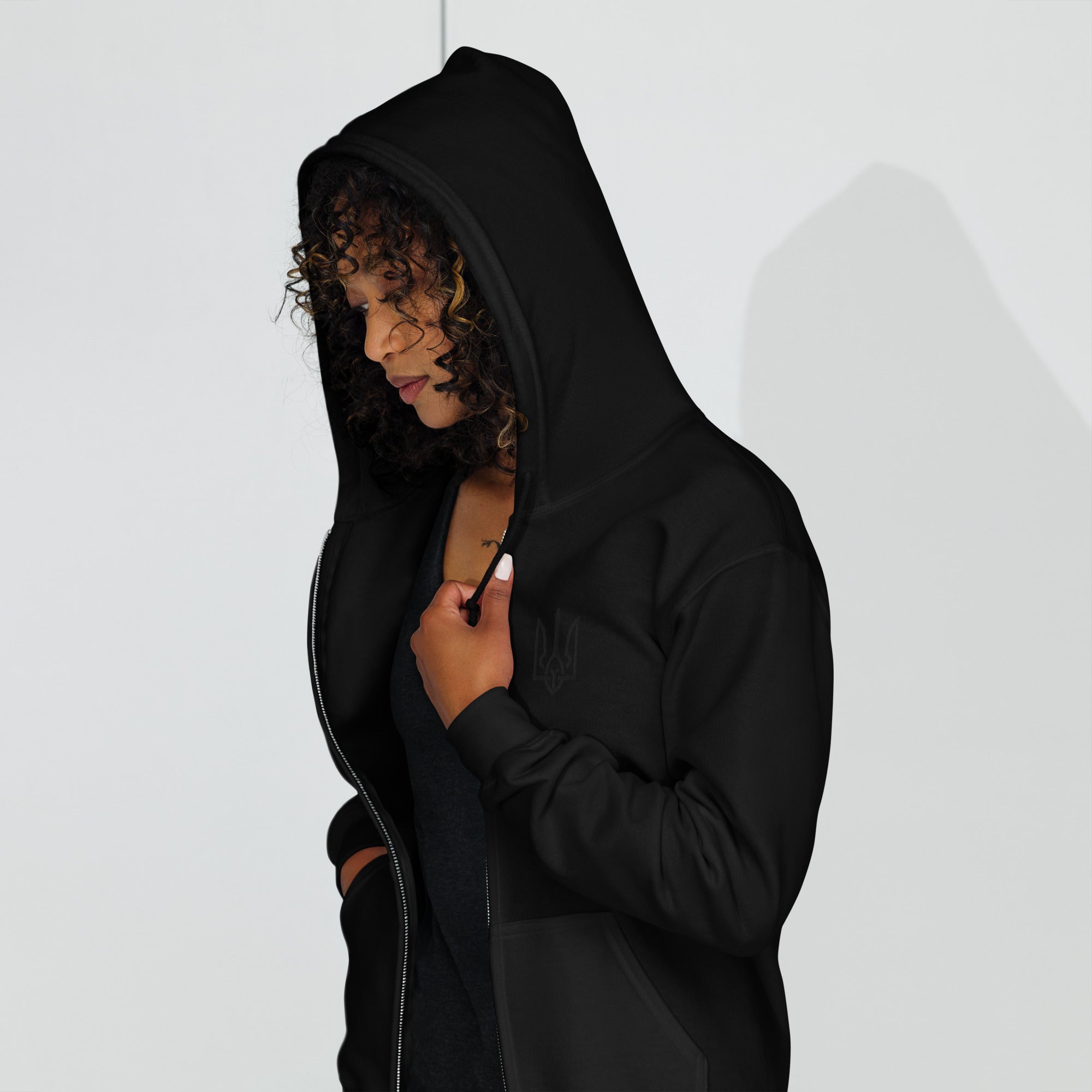 Woman wearing a black heavy blend zip hoodie with Ukrainian Tryzub design, showing soft fleece lining and tailored fit.