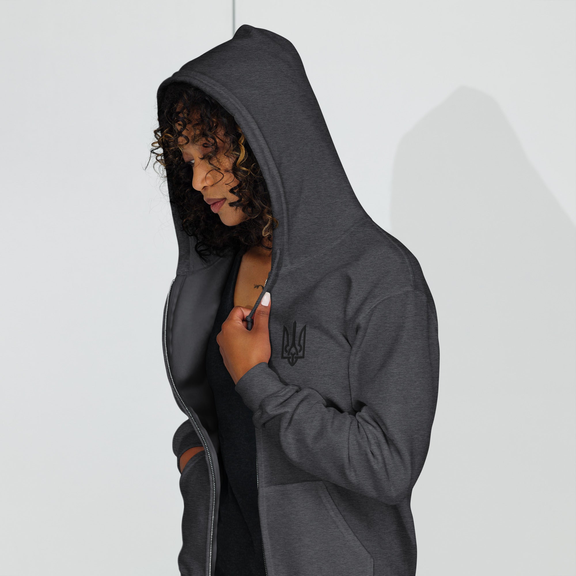 Woman wearing a dark gray zip hoodie with Ukrainian Tryzub design, showcasing cozy fleece lining and tailored fit.