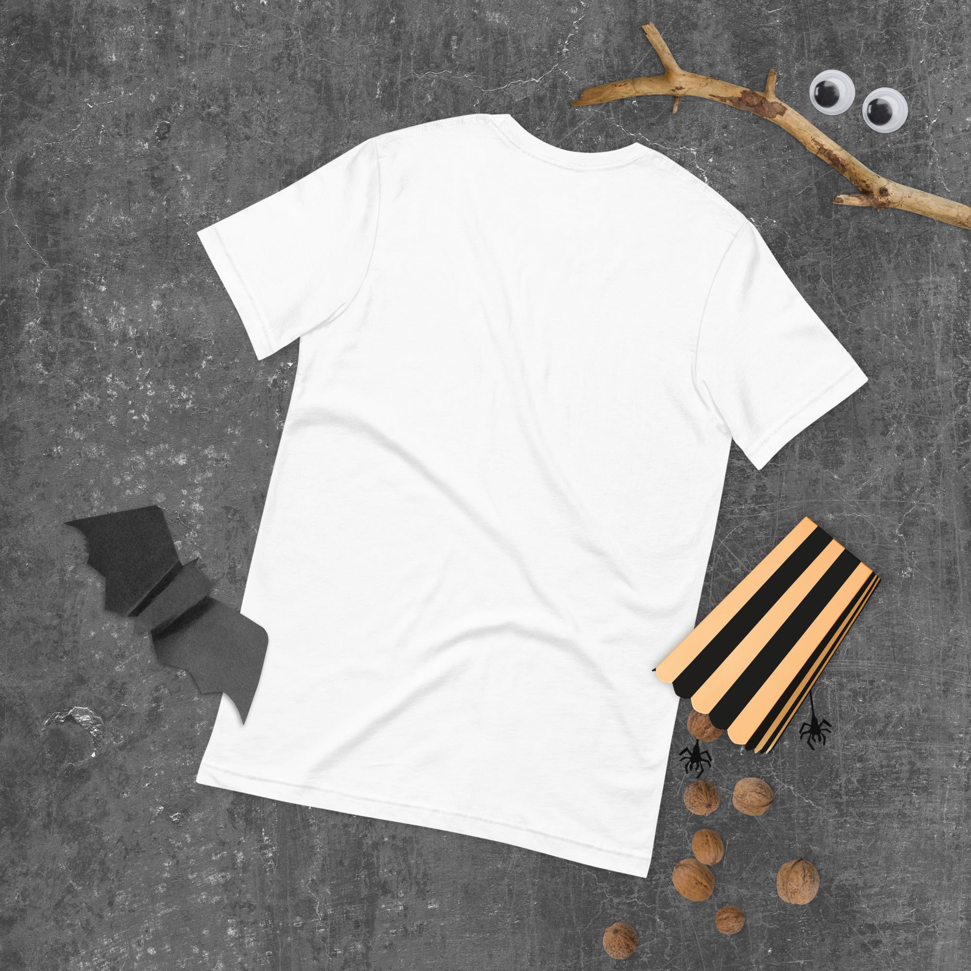 Back view of a plain white T-shirt on a dark textured background with Halloween decorations including walnuts and paper bats.