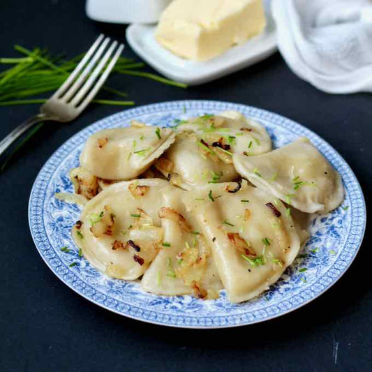 Plate of homemade Ukrainian varenyky dumplings with onion topping and a fork on the side, perfect for traditional meals.