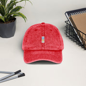 Red vintage cotton twill cap with embroidered Ukrainian Tryzub, featuring a washed-out effect and adjustable brass buckle, displayed on a desk.
