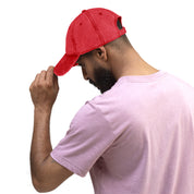 Man wearing red vintage cotton twill cap with embroidered Ukrainian Tryzub, adjusting brim, side profile view.