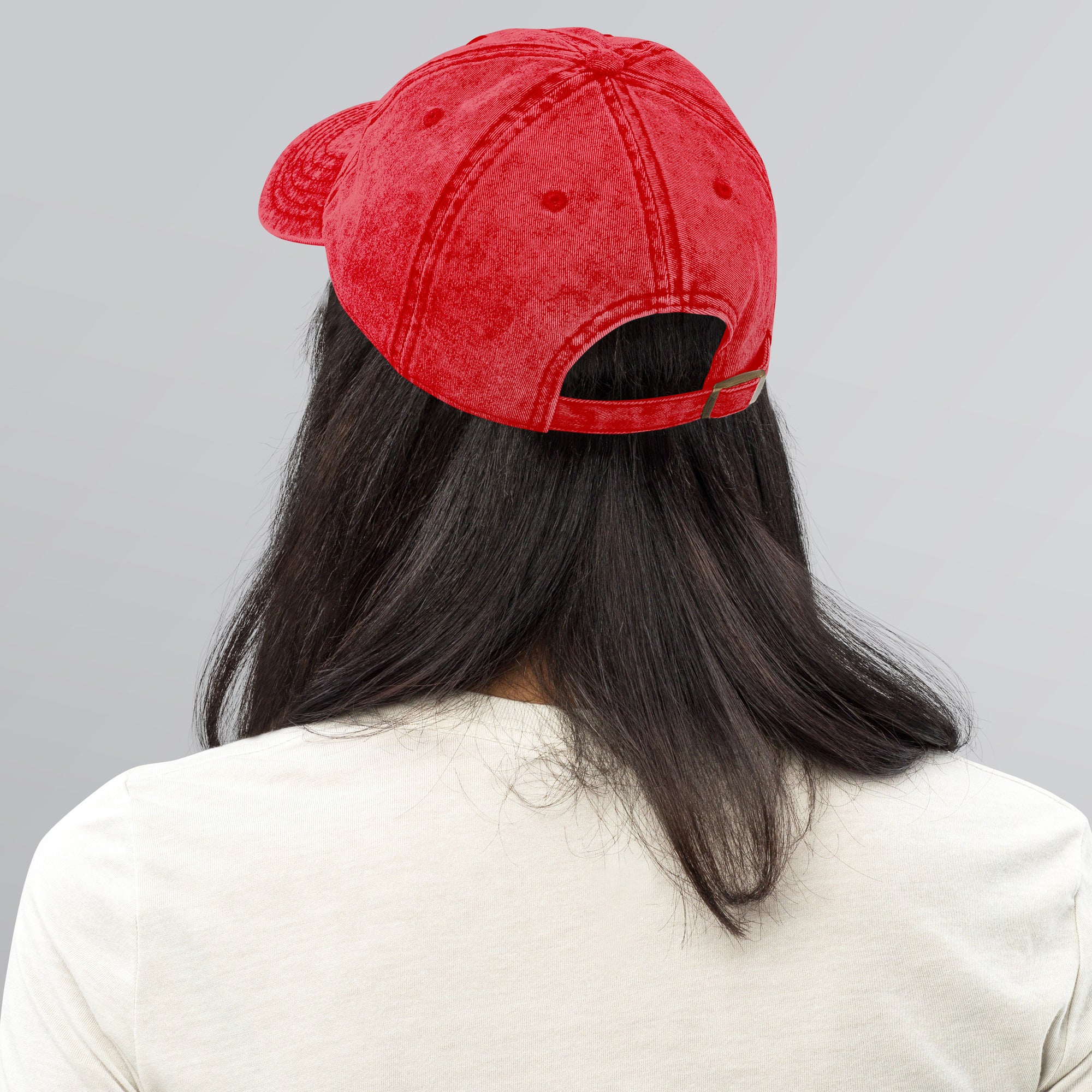 Person wearing red vintage cotton twill cap with adjustable brass buckle, showcasing back view and washed-out texture.