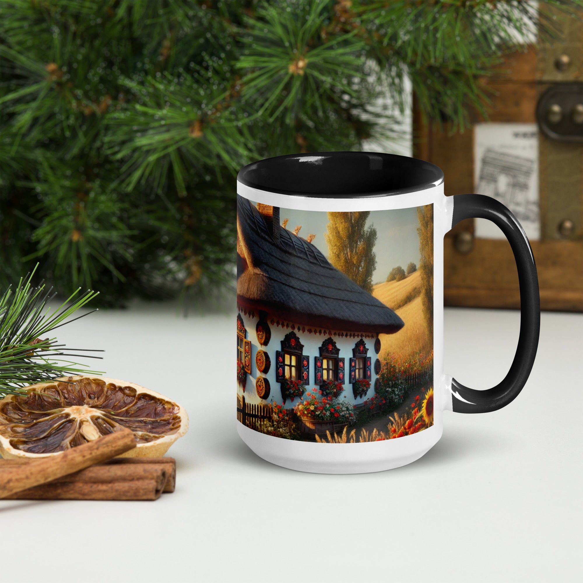 Ceramic mug with Ukrainian cottage and scenic yard design, featuring black rim and handle, surrounded by pine branches and dried orange slices.