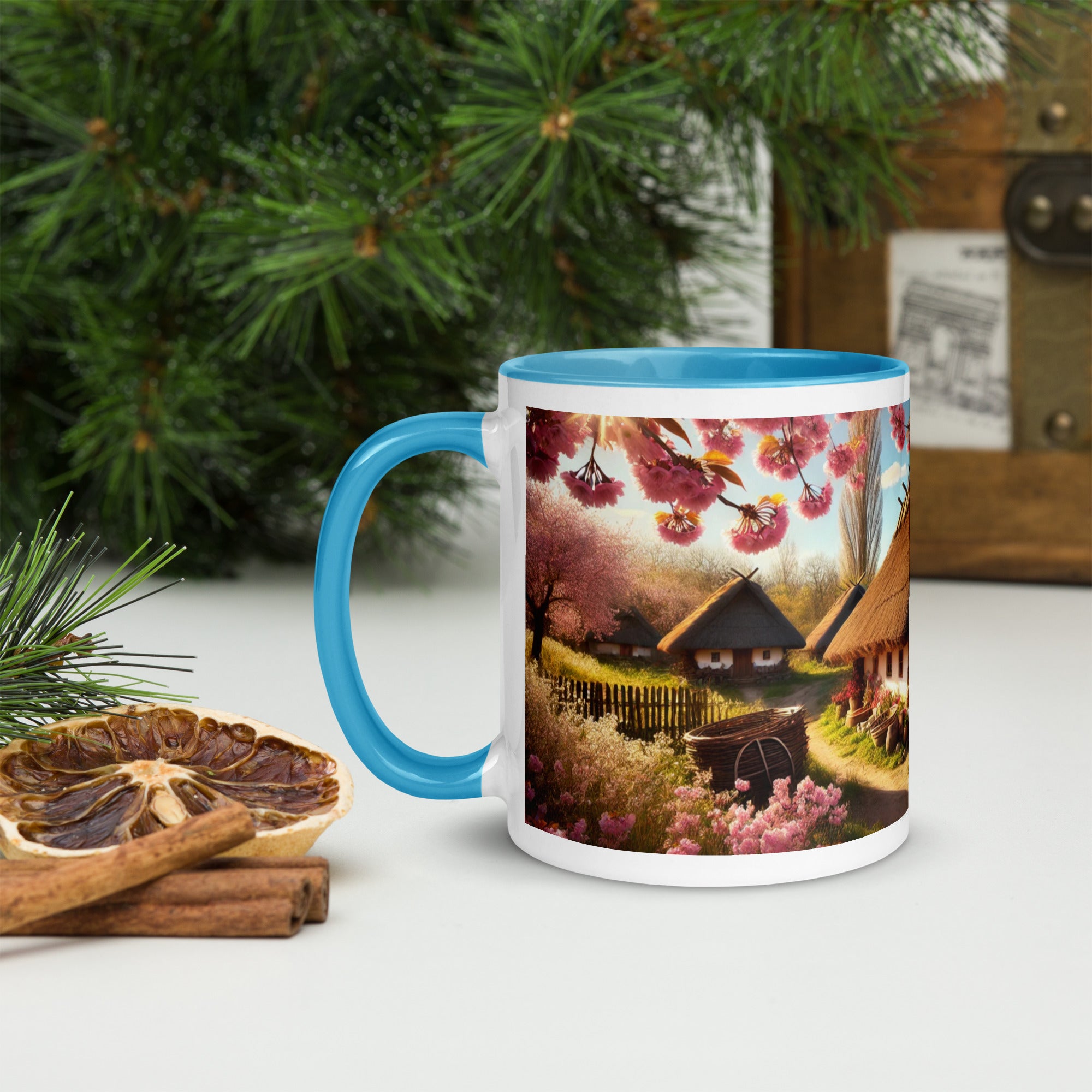 Ceramic mug with Ukrainian cottage and cherry orchard design, blue rim and handle, on a table with pine and dried fruit.