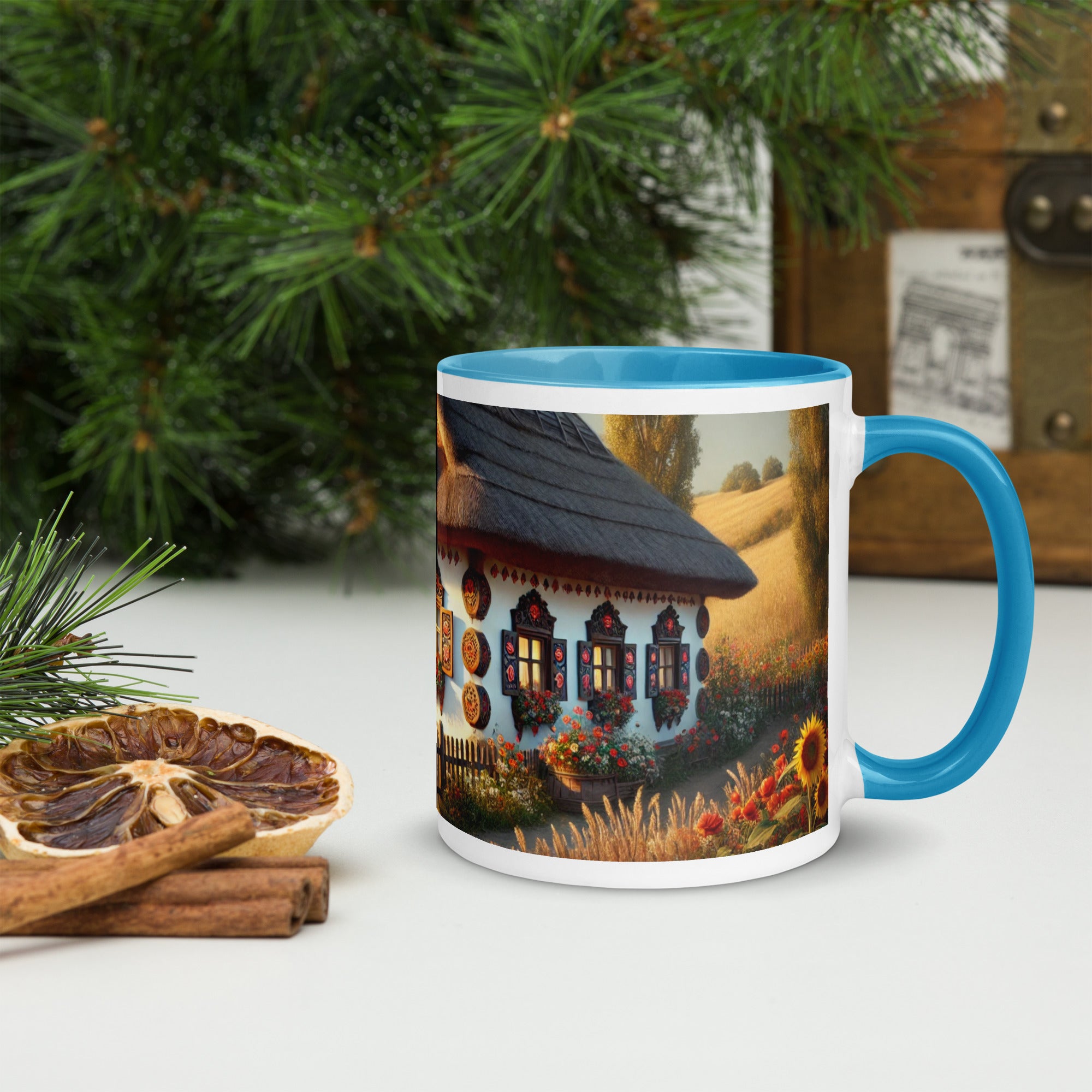 Ceramic mug featuring a Ukrainian cottage with scenic yard, blue rim and handle, surrounded by dried citrus and pine branches.