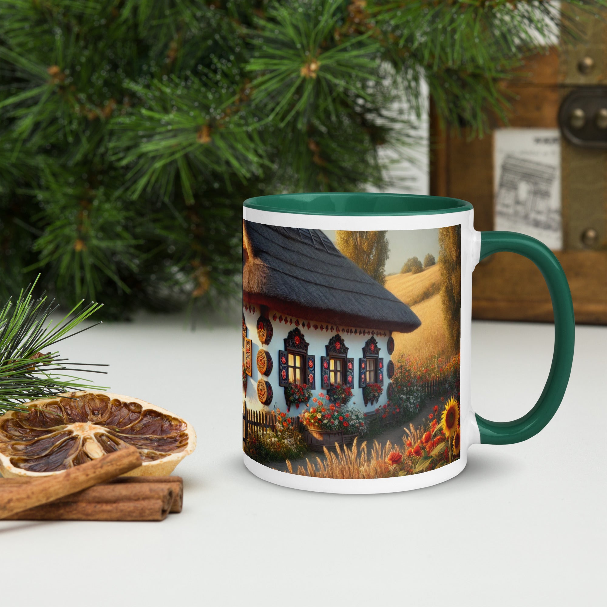 Ceramic mug featuring Ukrainian cottage and scenic yard, with green rim and handle, surrounded by festive greenery and dried oranges.