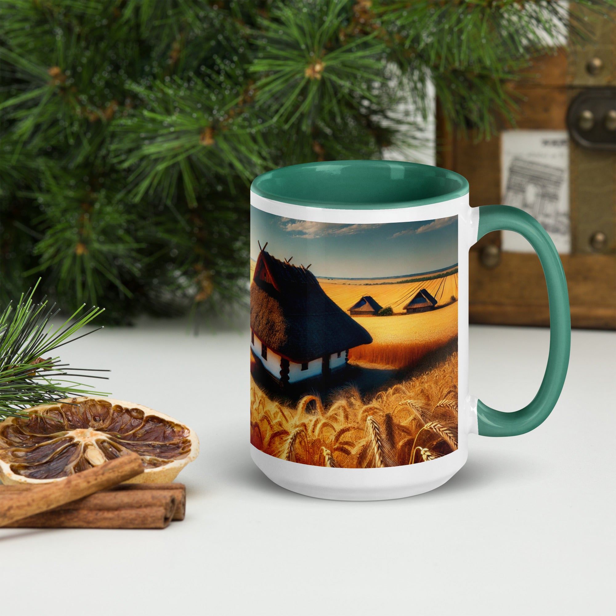 Ceramic mug featuring a Ukrainian cottage in a wheat field design, with a green rim and handle, placed on a white table near dried citrus.