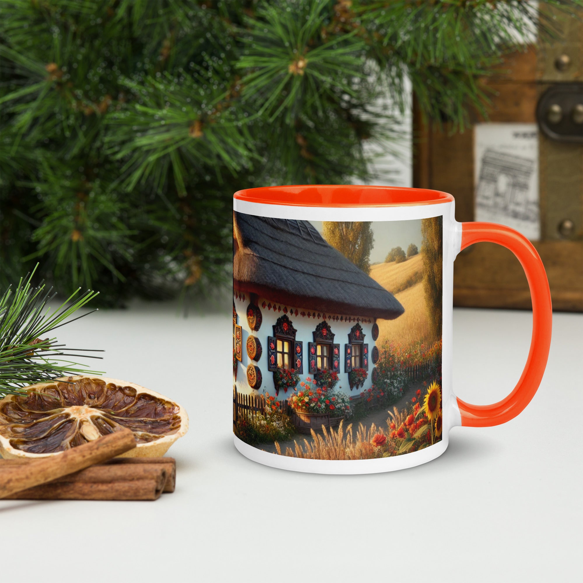 Ceramic mug with Ukrainian cottage and scenic yard design, featuring an orange rim and handle, surrounded by greenery.