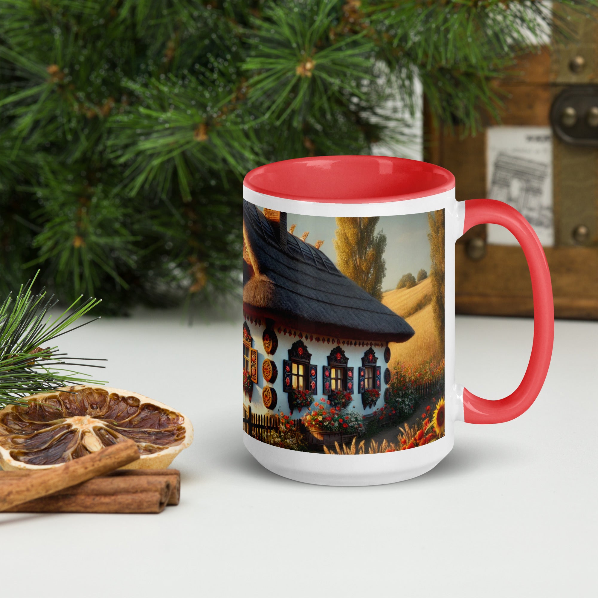Ukrainian cottage ceramic mug with scenic yard design, red interior and handle, next to dried citrus and pine branches.