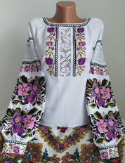 White homespun vyshyvanka blouse with traditional Ukrainian embroidery, featuring purple floral patterns on sleeves and front.