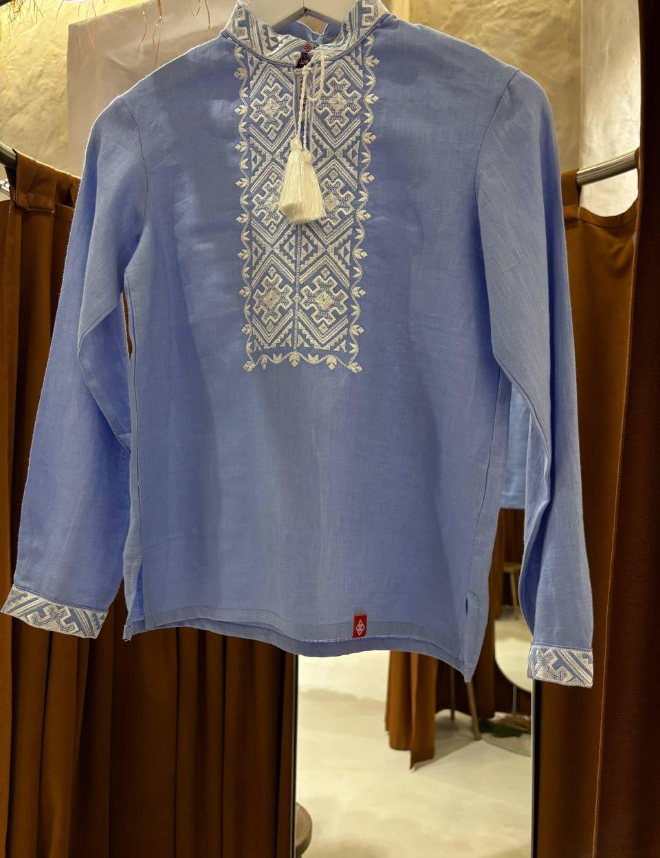 Blue linen shirt with white embroidered Ukrainian motifs, long sleeves, displayed against a neutral background.