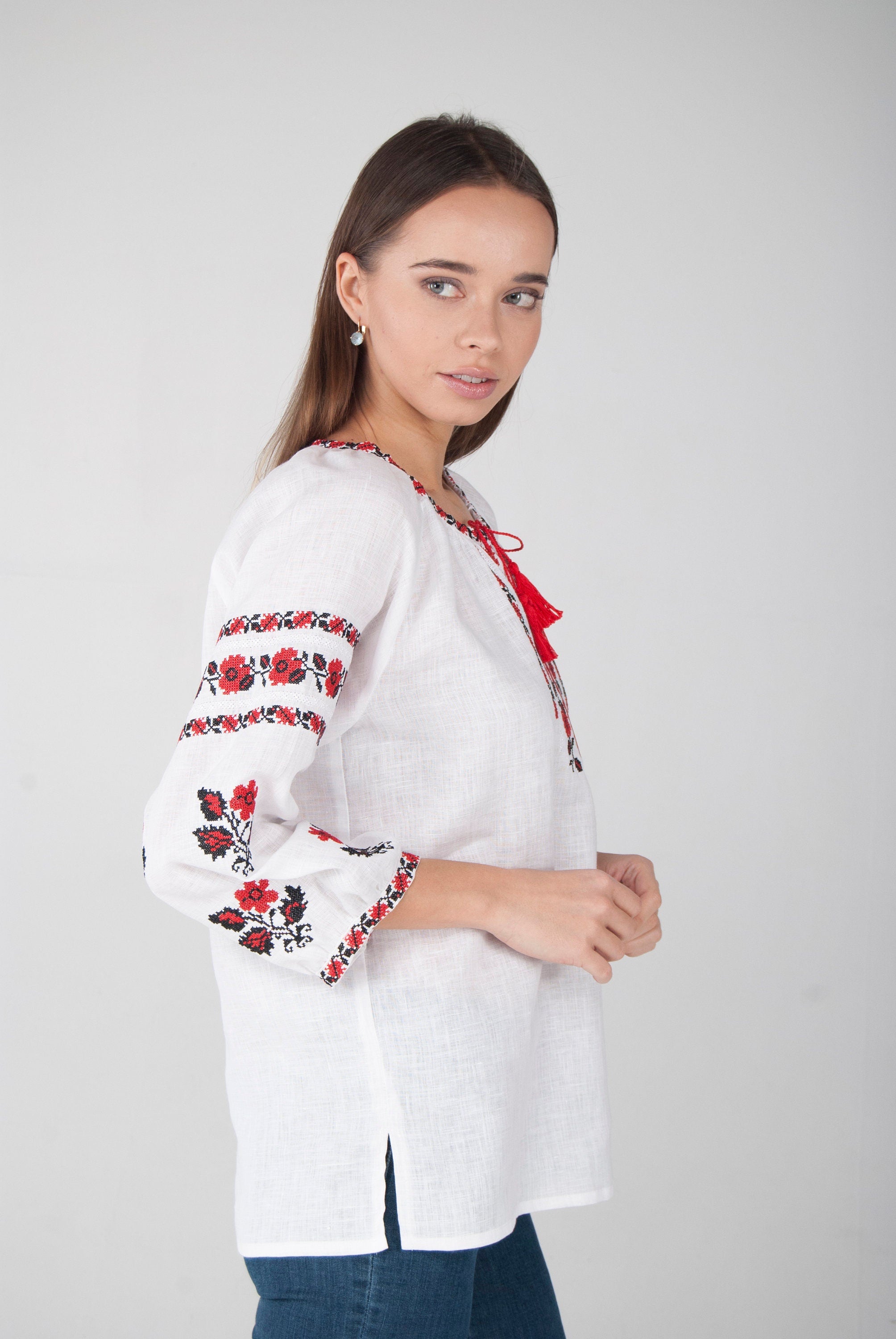 Woman wearing white linen vyshyvanka blouse with red Ukrainian embroidery, three-quarter sleeves, and vibrant folk design