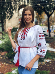 Woman wearing white linen Vyshyvanka blouse with red embroidery, Ukrainian folk shirt, standing outdoors.