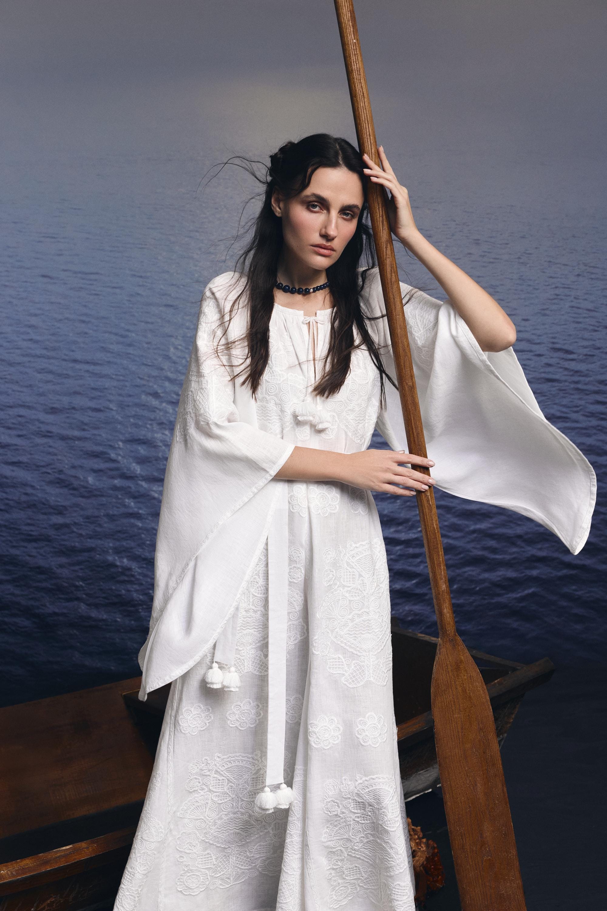 White linen boho wedding dress with Ukrainian embroidery, modeled near water.