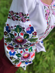 White Ukrainian embroidered blouse with colorful floral motifs on homespun fabric, showcasing traditional women's vyshyvanka design.