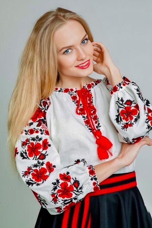 Woman wearing a traditional Ukrainian embroidered blouse with red and black floral patterns on white fabric.