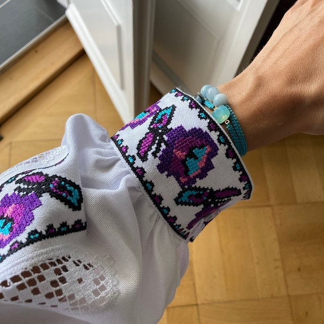 Purple and turquoise embroidered cuff detail on white Ukrainian vyshyvanka blouse, showcasing traditional cross-stitch patterns.