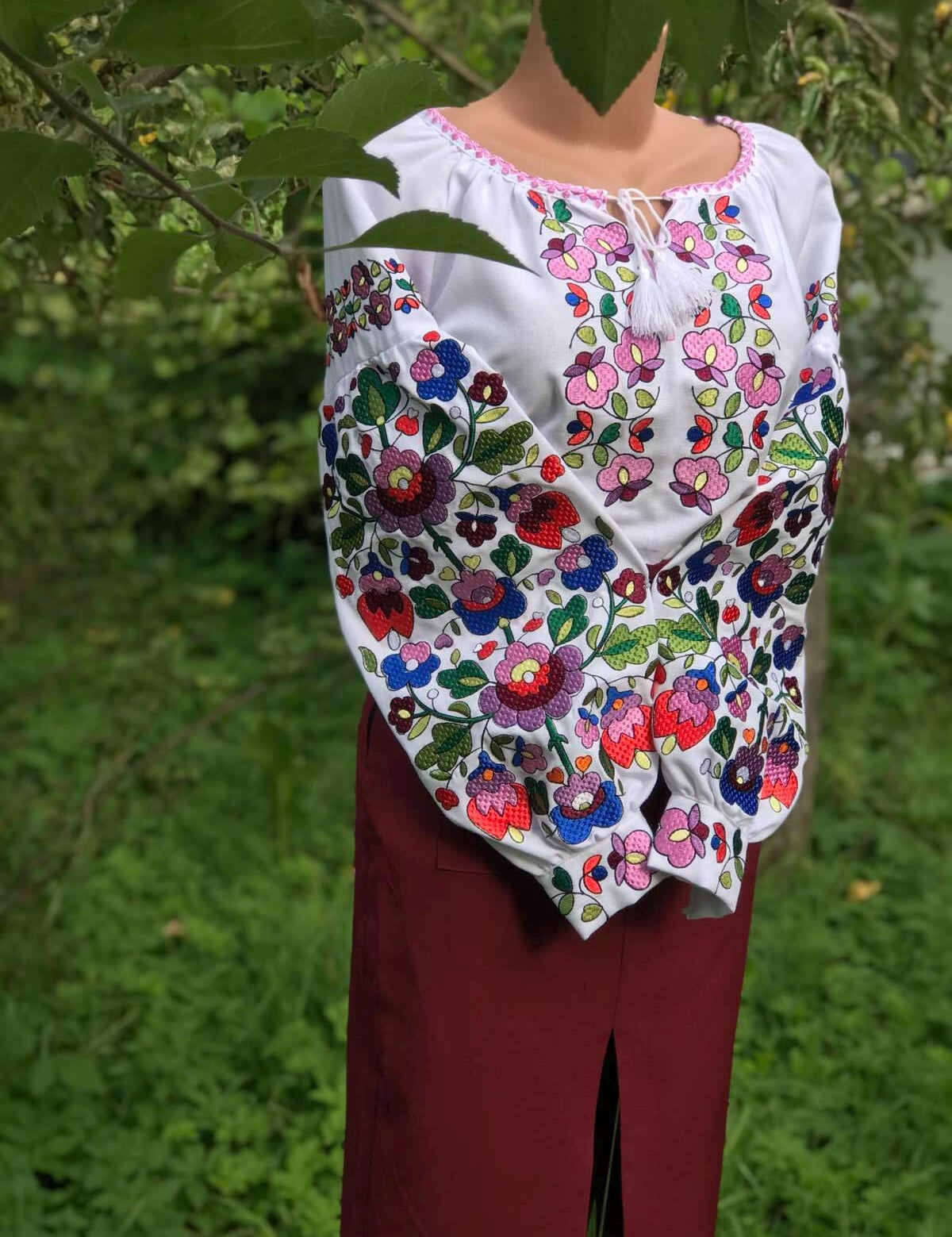 Women's white embroidered vyshyvanka blouse with Ukrainian folk motifs on homespun fabric, shown outdoors.