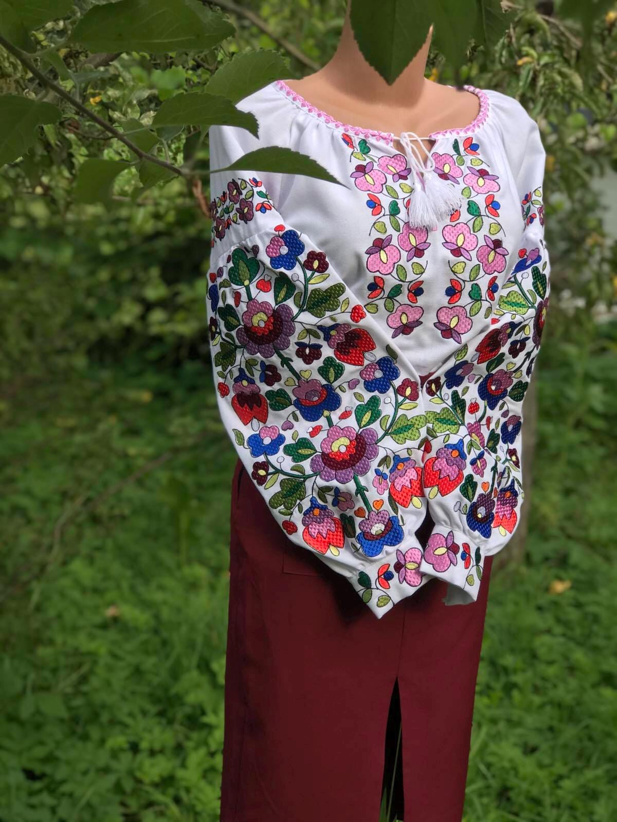 Women's white embroidered vyshyvanka blouse with Ukrainian folk motifs on homespun fabric, shown outdoors.