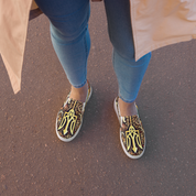 Woman wearing slip-on canvas shoes with Ukrainian symbols and jeans on a sidewalk.