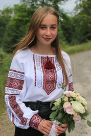 Woman in traditional cotton vyshyvanka blouse with Ukrainian folk embroidery holding a bouquet of flowers outdoors.