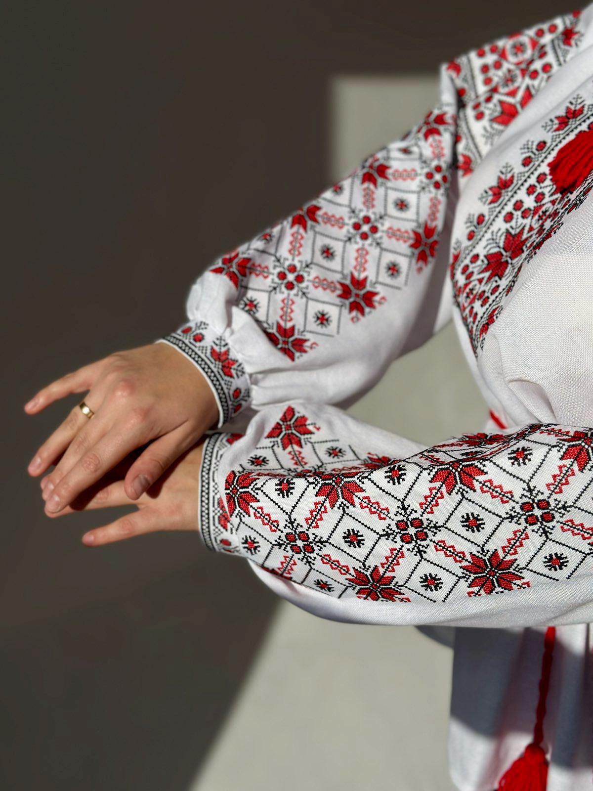 Close-up of a woman's arm wearing a traditional Ukrainian Vyshyvanka blouse, featuring red and black embroidered folk patterns on white fabric.