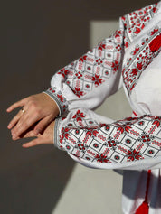 Close-up of a woman's arm wearing a traditional Ukrainian Vyshyvanka blouse, featuring red and black embroidered folk patterns on white fabric.