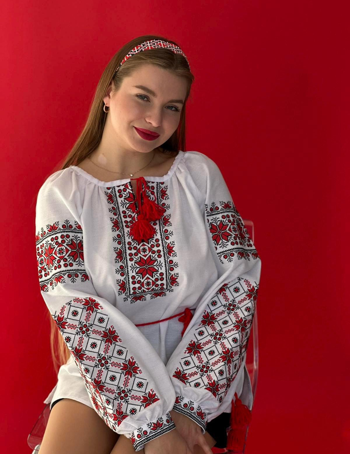 Woman wearing a Ukrainian Vyshyvanka embroidered blouse, featuring red and black folk patterns on white homespun fabric.
