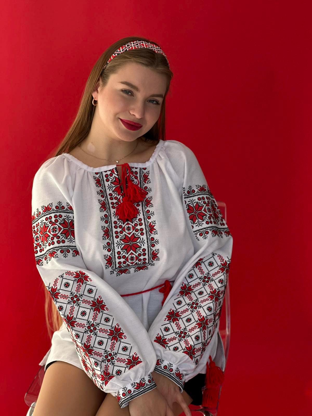 Woman wearing a Ukrainian Vyshyvanka embroidered blouse, featuring red and black folk patterns on white homespun fabric.