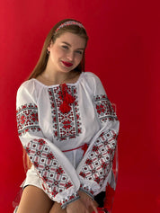 Woman wearing a Ukrainian Vyshyvanka embroidered blouse, featuring red and black folk patterns on white homespun fabric.