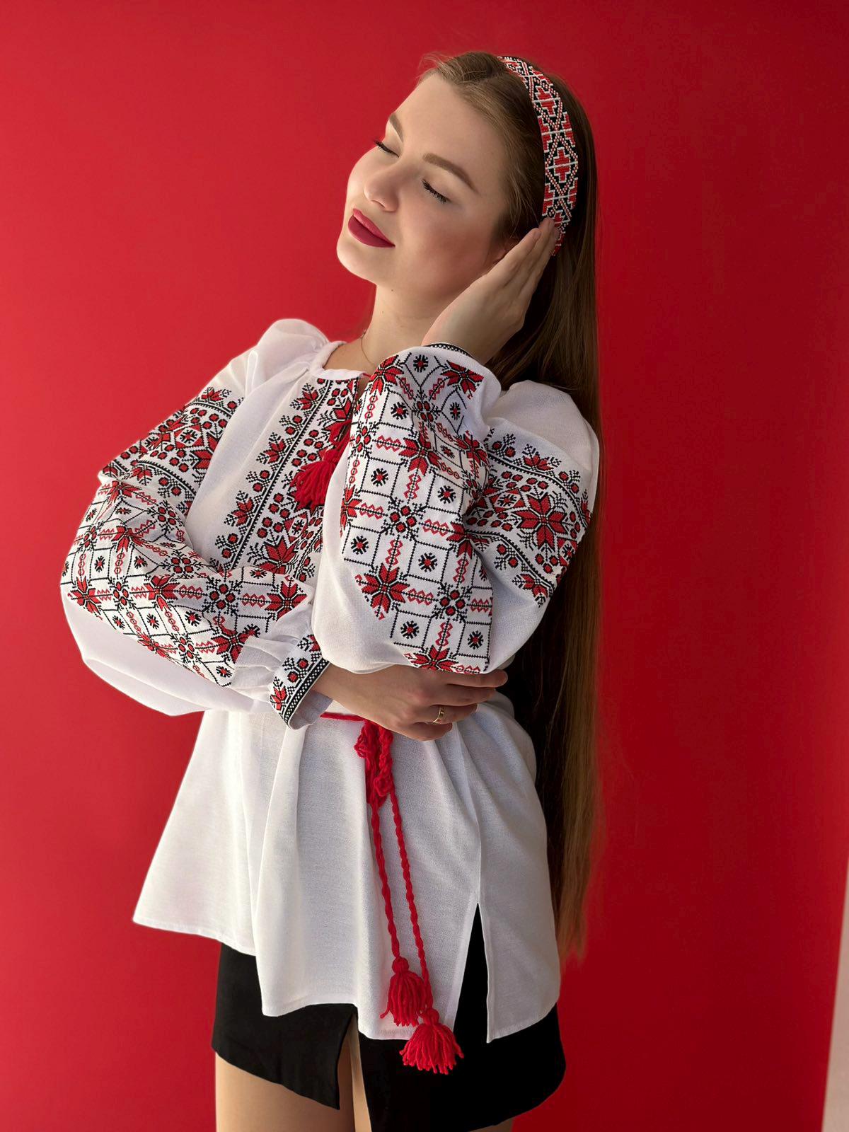 Woman modeling traditional Ukrainian embroidered blouse with red patterns on white fabric.