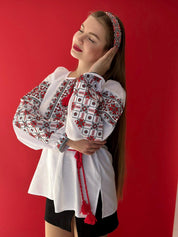 Woman modeling traditional Ukrainian embroidered blouse with red patterns on white fabric.