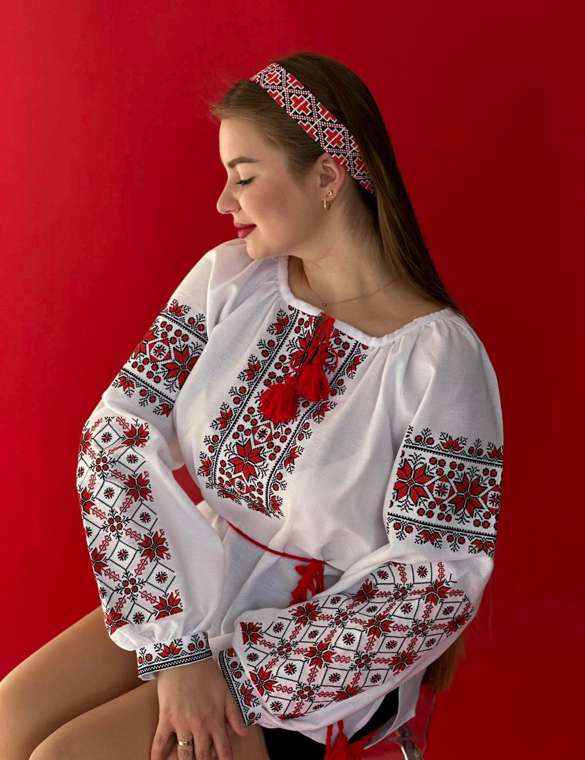 Woman wearing red and white embroidered Ukrainian Vyshyvanka blouse with matching headband on a red background.